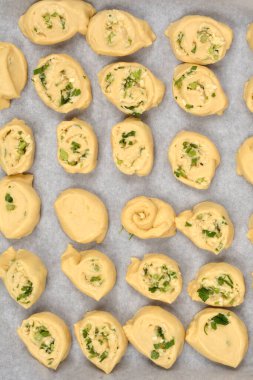 Tepeden çekilen fotoğrafta parmesan, sarımsak ve maydanozla dolu sayısız hamur rulosu var. Parşömen kağıdıyla kaplanmış bir fırın kağıdına dizilmiş.
