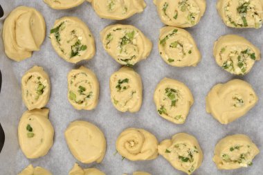 Tepeden çekilen fotoğrafta parmesan, sarımsak ve maydanozla dolu sayısız hamur rulosu var. Parşömen kağıdıyla kaplanmış bir fırın kağıdına dizilmiş.