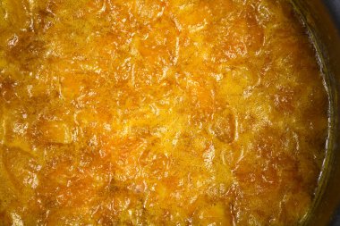 Yakından bakınca parlak turuncu mandalinalı marmelatların metal bir tencerede pişirildiğini ve doğranmış meyve parçalarını ön plana çıkardığını görüyoruz.