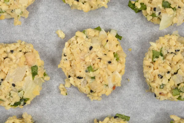 Daha çok doğranmış soya fasulyesi, soğan ve otlardan yapılan çiğ vejetaryen köfteleri, parşömen astarlı pişirme tepsisi üzerinde pişirilmeye hazırdır.