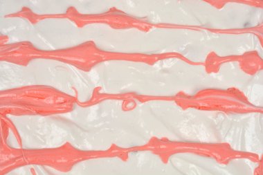 Detaylı, tam kare bir çekim kalın, beyaz bir krema yüzeyinde parlak pembe katmanlı dalgalı çizgiler gösteriyor.