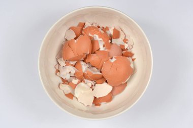 Beyaz bir kase, yukarıdan bakıldığında düz beyaz ya da açık gri bir zemin üzerine kurulmuş kırık kahverengi ve beyaz yumurta kabuklarıyla doludur.