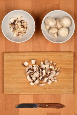 Beyaz kaselerde ve tahta kesme tahtasının üzerinde bıçakla kesilmiş taze mantarlardan oluşan bir kare.