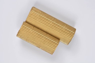 Tepeden çekilen iki silindirik, metalik altın kıvrımlı karton parçası beyaz arka planda üst üste biniyor.