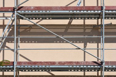 Açık kahverengi bir binanın ön cephesinde metal iskelenin bir bölümü duvarda gölgeler bırakıyor.