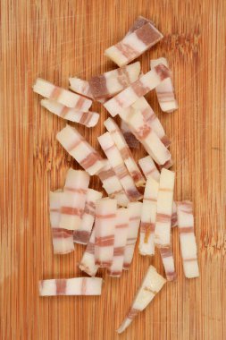 Düzensiz bir şekilde doğranmış domuz pastırması parçaları bambu tahtaya saçılmış.