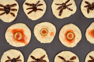 Çiğ hamurdan yapılmış, zeytin dilimleri ve domates sosuyla kaplı, göz küresi ya da örümcek etkisi için pişirilmemiş Cadılar Bayramı aperatifleri.