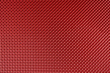 Kabartmalı kırmızı metal bir yüzeye ait makro bir fotoğraf, muhtemelen bir kabartma levhası ya da tepsisi, bir üniforma, küçük girintili elmas şekillerinin tekrarlanan deseni