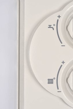 Dikey yakın plan, su ve radyatör sıcaklık kontrolü sembolleri ile minimum ile maksimum arasında değişen bir termostat veya kontrol ünitesinin açık gri plastik panelini gösterir.