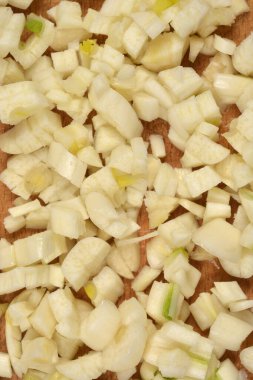 Dar, tepeden tırnağa yakın plan, bazılarının hafif yeşil renkte, ahşap bir yüzey üzerinde taze doğranmış sarımsak parçalarını gösteriyor.