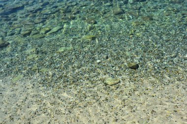 Berrak turkuaz su, karışık kum, küçük çakıl taşları ve daha büyük kayalardan oluşan bir deniz yatağını kaplayarak doğal bir eğilim yaratır.