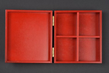 Açık, kare, ahşap bir kutu. İç kısmı kırmızı ve dört bölmesi koyu gri bir arka planda sergileniyor.