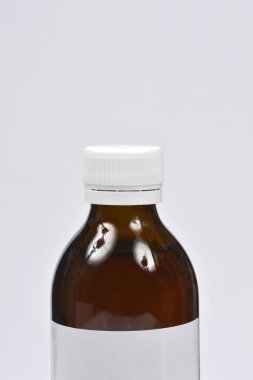 Kahverengi cam bir şişenin tepesine yakın çekim, muhtemelen öksürük şurubu içeriyor, açık gri arka planda beyaz bir kaburga kapağı var.