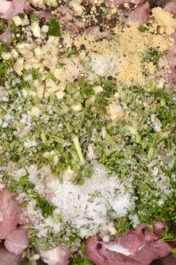 Ağır bir şekilde tuz, doğranmış sarımsak, tam biber, kurutulmuş baharat ve taze yeşil maydanozla tatlandırılmış metal bir kasedeki çiğ domuz eti.