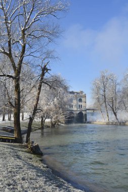 Ozalj 'daki Slava Raskaj yüzme alanındaki Kupa Nehri' nin manzaralı kış manzarasında, don kaplı ağaçlar ve parlak mavi gökyüzünün altındaki tarihi Munjara hidroelektrik santrali yer alıyor.