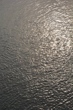 Dalgalanan Sava nehri su yüzeyinin dikey, yakın çekim görüntüsü parlak, gümüş-altın bir güneş ışığını yansıtıyor.