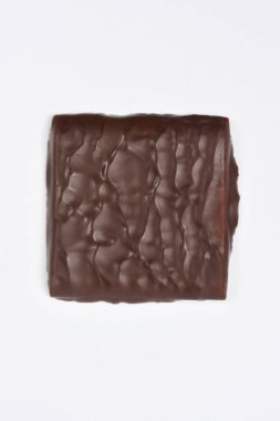 Koyu renkli, dalgalı bir yüzeyi olan tek bir çikolatalı şekerleme kare temiz beyaz bir arkaplan üzerine kuruludur.