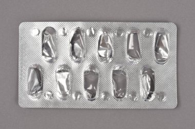 Bir zamanlar gri bir arka plana yerleştirilmiş, içinde on hap bulunan boş gümüş su toplayıcı paketinin yakın plan, yatay bir çekimi.