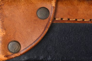 Eski deri bir valizin yakın plan çekimi koyu renkli, dokulu siyah bir kumaşı üst üste bindiren iki perçinli kavisli kahverengi deri kayışı gösteriyor.