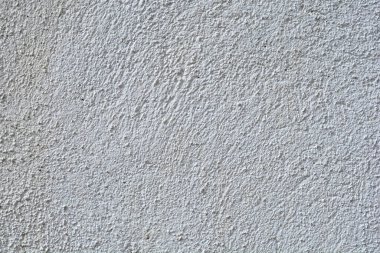 Yakın çekim, beyaz ya da açık gri bir duvar yüzeyinin pürüzlü, aynı kaba dokusunu doğal ışık altında yakalar.