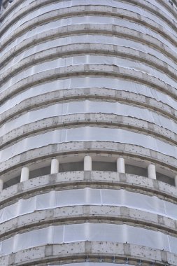 Yüksek silindirik beton bir bina, inşaat aşamasında beyaz koruyucu ağ katmanlarıyla kaplıdır.