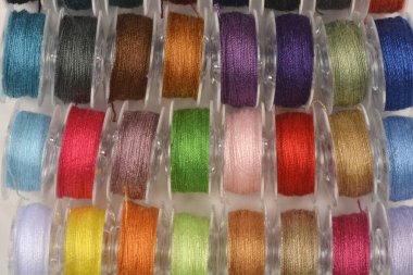 A top-down view of many transparent plastic bobbins neatly wound with a wide spectrum of colorful threads for sewing and textile projects