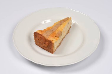 Dekoratif kabuklu fırında pişirilmiş peynirli kek, arka planda beyaz bir tabakta servis edilir.