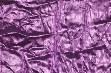 Metalik parıltılı buruşuk parlak mor kumaş dinamik dokulu bir arka plan yaratır.