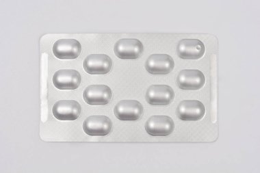 Üzerinde oval şekilli birkaç hap bulunan gümüş bir alüminyum su toplayıcı paketi açık gri bir arka plan üzerine kuruludur.