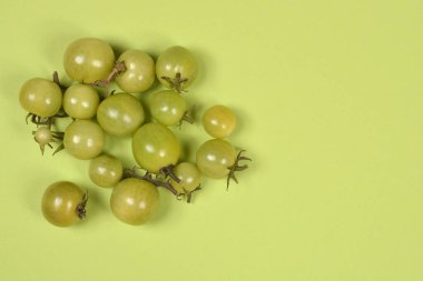Bir grup olgunlaşmamış yeşil kiraz domatesinin fotokopi uzayı eşleşen yeşil kağıt arka planına serpiştirilmiş en iyi stüdyo resmi.
