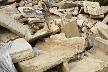 Dağınık beton levhalar ve inşaat enkazı paslı metal takviyeleri ve yıkım alanının çeşitli gri dokularını gösteriyor.