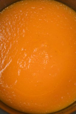 Yüksek açılı tam çerçeve çekimi bir tencerenin içindeki canlı turuncu havuç çorbasının pürüzsüz ve kalın tutarlılığını gösteriyor.