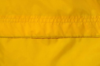 Parlak sarı sentetik kumaş dokusunun yakın plan çekimi ince dokuma ve yatay çift dikiş..