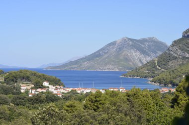 Zuljana köyünün kırmızı çatılı evlerini barındıran güzel bir kıyı manzarası. Yeşil tepeler ve Peljesac yarımadasındaki dağlarla çevrili bir turkuaz körfeze kurulmuş.
