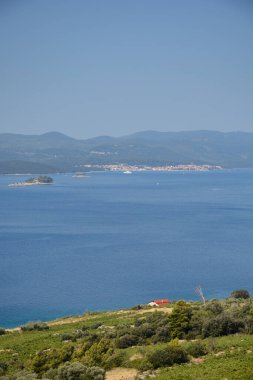 Peljesac 'ın yeşil yamaçlarından mavi denizi aşıp Korcula kasabasına ve uzak dağlara bakan güneşli bir manzara.