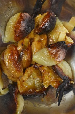 Kavrulmuş sarımsak karanfillerinin zengin dokusunu ve altın rengi ve metal bir kasenin içinde kömürleşmiş kenarlarını gösteren bir makro yakın çekim görüntüsü.