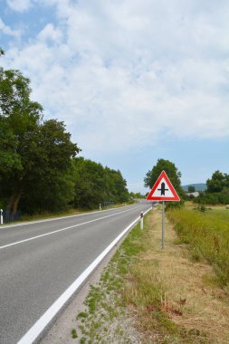 Yeşil araziden Korenica 'nın kuzeyine doğru giden kavşak işareti olan asfalt yol manzarası