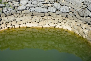 Cista Velika yakınlarındaki Crljivica arkeoloji sahasında eski taş duvarların ve ortaçağ kuyusunun yeşil renkli sularının yakın çekimi.