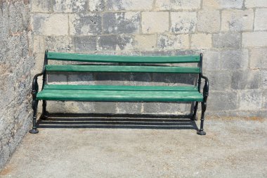Akdeniz 'de eski dokulu taş bir duvara karşı duran siyah demir bacaklı klasik ahşap bir bank.