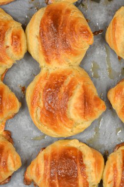 Yukarıdan bakıldığında, fırından çıktıktan sonra gri parşömen kağıdına yerleştirilmiş parlak kabuklu taze, kahverengi hamur işleri görülüyor..