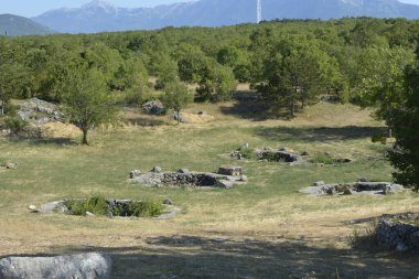 Geniş bir manzara, Cista Velika yakınlarındaki Crljivica arkeolojik sahasında çimenli bir alana yayılmış çok sayıda antik taş kuyusunu gösteriyor.