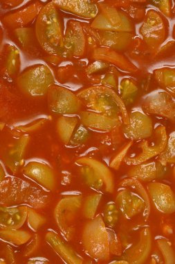 Kesilmiş yeşil domates ve soğan parçalarının bulunduğu kalın kırmızı domates sosunun yakın çekim görüntüsü bir tencerede pişiyor.