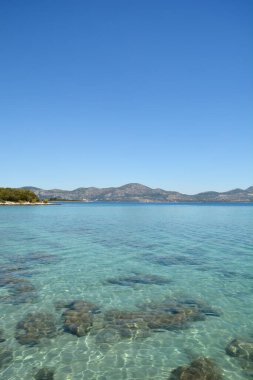 Peljesac yarımadasındaki Sreser 'deki şeffaf turkuaz Adriyatik Denizi' nin dikey çekimi, mavi bir gökyüzünün altında ufukta Hırvatistan 'ın dağları görünüyor.