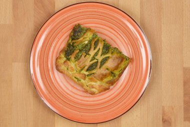 Ahşap bir masada portakal tabağında servis edilen fırında somon ve ıspanaklı böreğin genel manzarası.