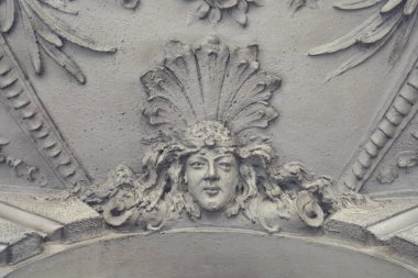 Eski bir mimari ön cephede tüylü bir başlıkla oyulmuş bir kadın yüz süsü.