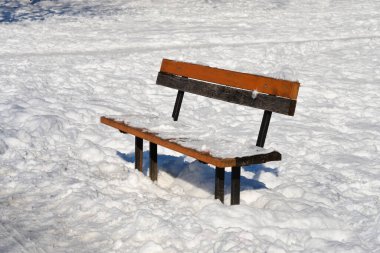 Bir ahşap park bankında kısmen beyaz kar altında parlak bir kış günü gömülü durur..