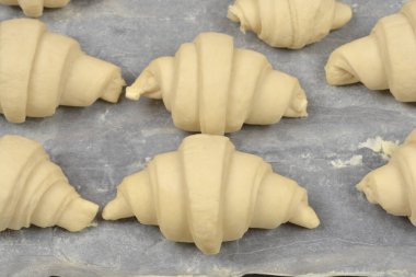 Pişmemiş hamur sıralarının üst görüntüsü. Hilal şeklinde hamurlar ya da kruvasanlar pişirmeden önce gri parşömen kağıdının üzerinde dinleniyor.