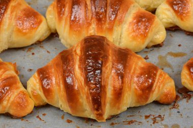 Yeni pişmiş birkaç altın rengi kruvasanın yan görüntüsü. Parşömen kağıdıyla birlikte fırında pişirme tepsisinin üzerinde çıtır çıtır bir kabuk var.