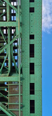 Yeşil boyalı çelik demiryolu köprüsünün alçak açılı görüntüsü. Karmaşık perçin detayları ve bulutlu mavi gökyüzüne karşı destek kirişleri.