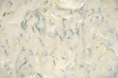 Ekşi krema, taze doğranmış yeşil dereotu ve doğranmış sarımsak parçacıklarından oluşan kalın beyaz bir dalgıcın ayrıntılı yakın plan görüntüsü.